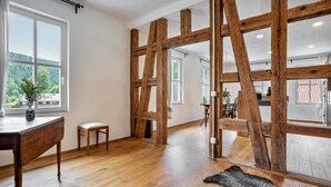 A room with wooden beams, a wooden table, a chair, a rug, and a window with a view of greenery.
