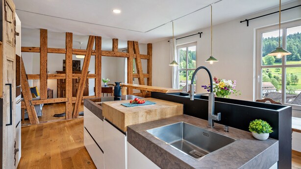A modern kitchen with a central island, a built-in sink, wooden beams, and a view of the outdoors.