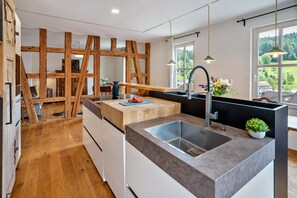 A modern kitchen with a central island, a built-in sink, wooden beams, and a view of the outdoors.