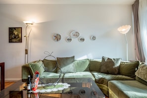 Un salon avec un canapé vert, une table basse en verre, des assiettes décoratives accrochées au mur et une lampe sur pied.