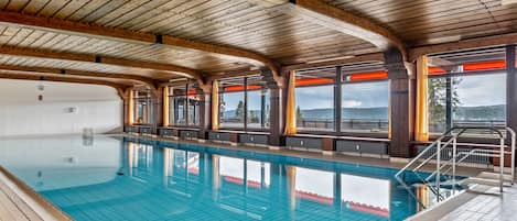Una piscina interior con vigas de madera, ventanas amplias y vistas al paisaje.