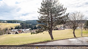 Un paysage rural avec un grand pin en évidence, un chemin pavé et des bâtiments situés au loin.