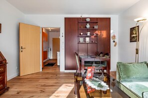 Un salon avec un plancher en bois, un canapé vert, une table à manger avec des chaises, un meuble en bois avec des étagères et un lampadaire.