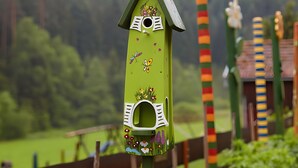 Une nichoir doté d’un toit vert et d’un panneau frontal blanc, décoré de fleurs et de papillons.