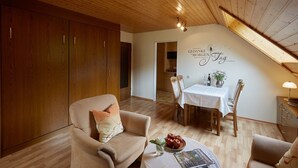 Une pièce chaleureuse avec un plancher en bois, une table à manger avec des chaises, un canapé avec des coussins et un mur orné d’une phrase décorative.