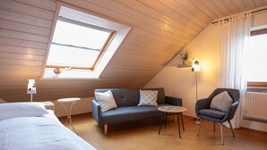 A room with a sloped ceiling, a sofa, a chair, a small table, and a bed. - Apartment 'Anne's' with Balcony and Wi-Fi (Bad Waldsee)