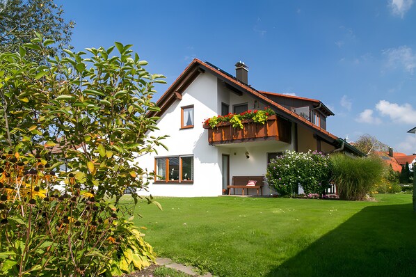 Une maison à deux étages avec un balcon, une pelouse bien entretenue et un ciel bleu dégagé.