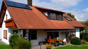 A house with a sloped roof, solar panels, a wooden bench, and a garden. - Apartment 'Anne's' with Balcony and Wi-Fi (Bad Waldsee)