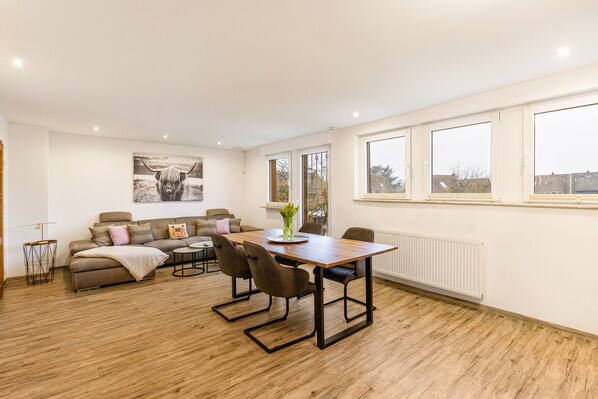En moderne stue med sofa, spisebord, stole, et stort vindue med udsigt og en radiator.