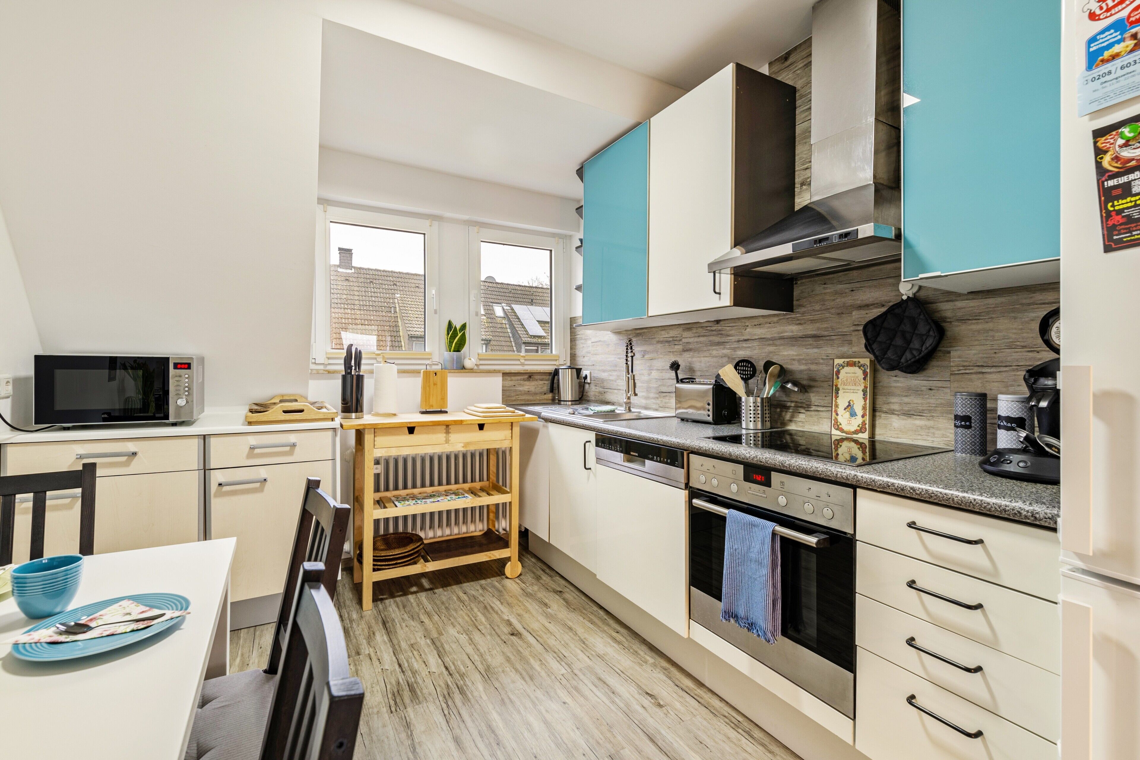 A modern kitchen with white and teal cabinets, a microwave, a coffee maker, and a wooden dining table.
