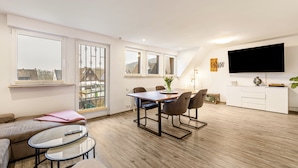 Un apartamento moderno con comedor, sofá, televisor y ventanas amplias.