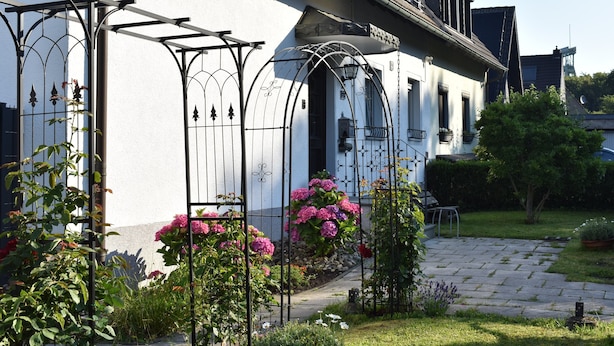 Un edificio con fachada blanca, un jardín de flores rosas y un sendero pavimentado.