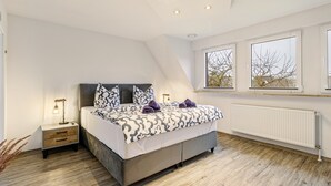 Un dormitorio con cama, mesitas de noche, lámpara, ventana y radiador.