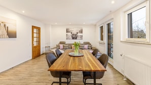 Un comedor moderno con una mesa de madera, sillas, un jarrón con flores y un sofá con cojines.