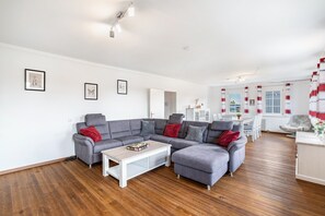 A modern living room with a grey sectional sofa, a white coffee table, and a dining area with a white table and chairs. - Holiday Home 'St Georg Stube' with Private Terrace, Private Garden and Wi-Fi (Grömbach)