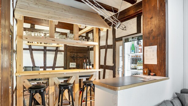 Un rústico espacio de bar con vigas de madera, taburetes y una barra llena de botellas.
