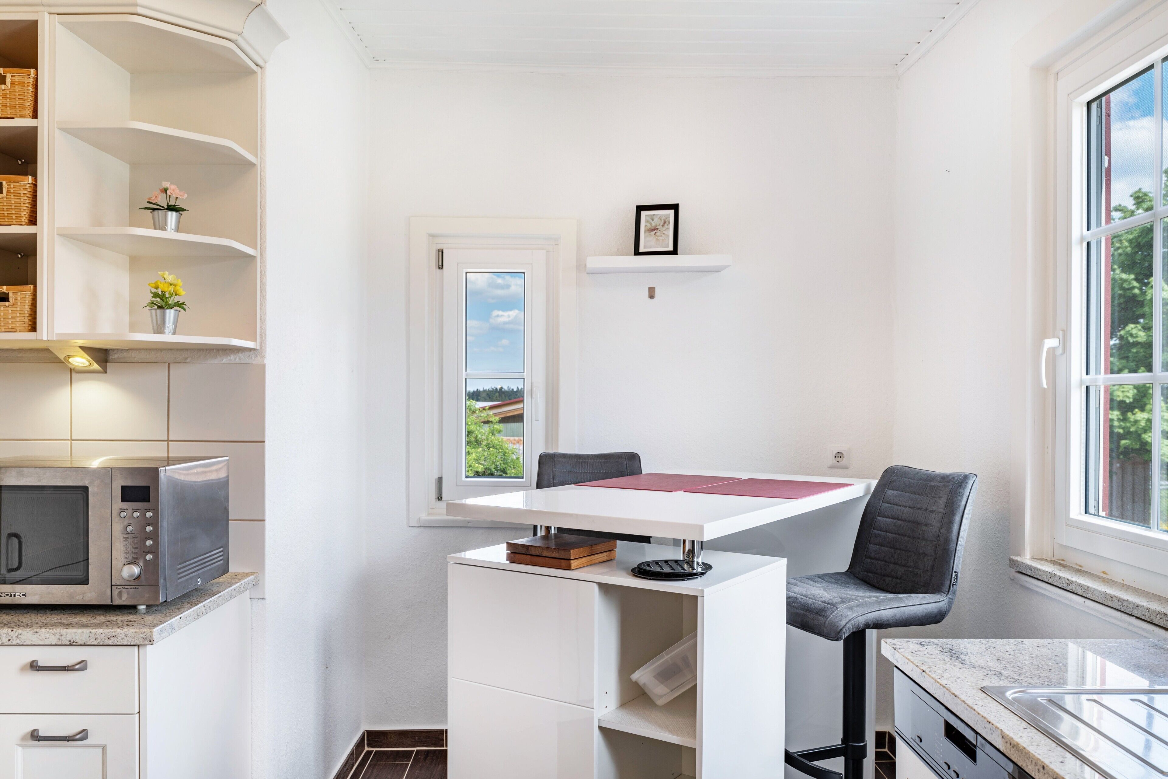 Een compacte keuken met een magnetron, een kleine tafel, een stoel en een raam met uitzicht.