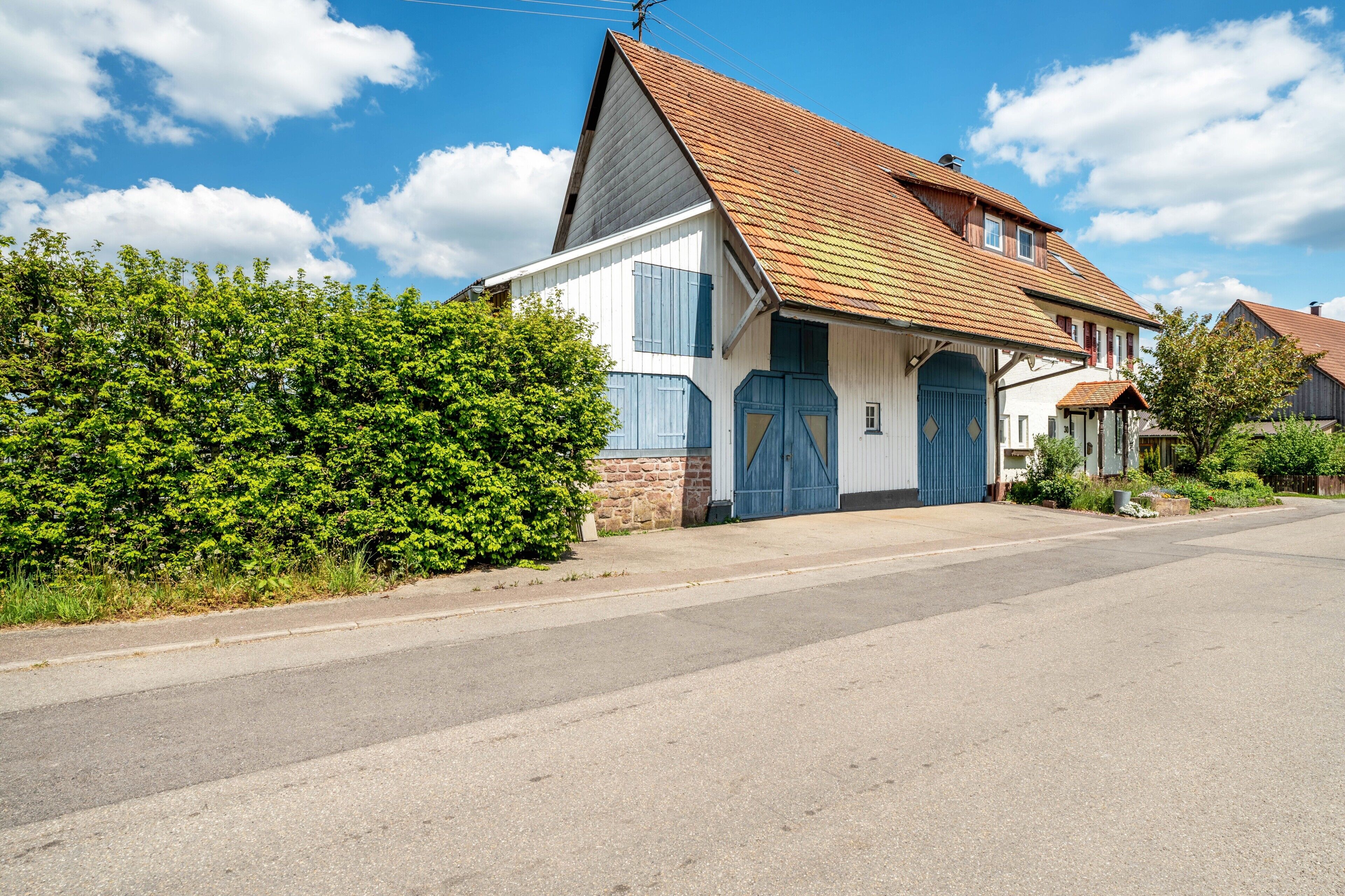 Ein zweistöckiges Haus mit geneigtem Dach, einer Veranda und einer großen, blauen Garagentür.