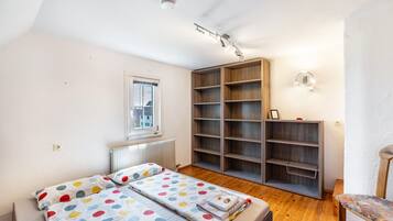 A bedroom with a bed, a window, a radiator, a bookshelf, and a chair.