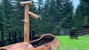 Uma cabana de troncos com uma torneira de metal, cercada por uma vedação metálica e árvores.