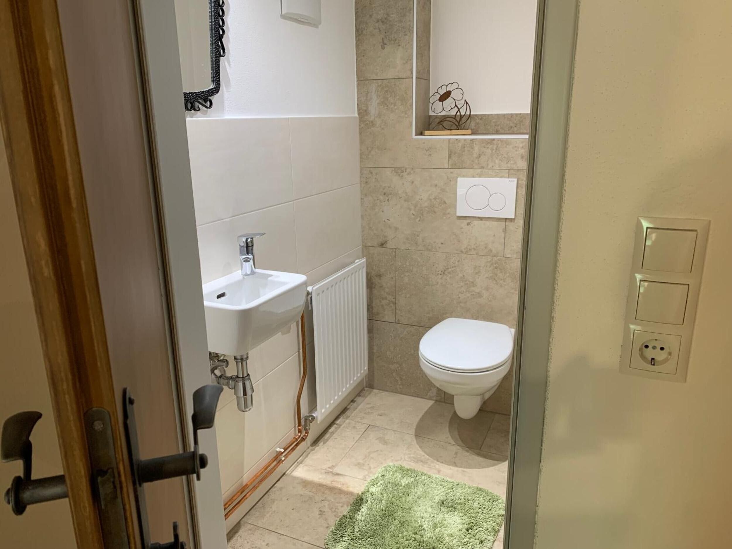 A bathroom with a white sink, a toilet, a radiator, and a green rug.
