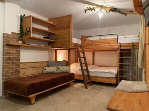 A bunk bed with a ladder, a sofa, and a small table in a room with wooden walls and a brick accent wall.