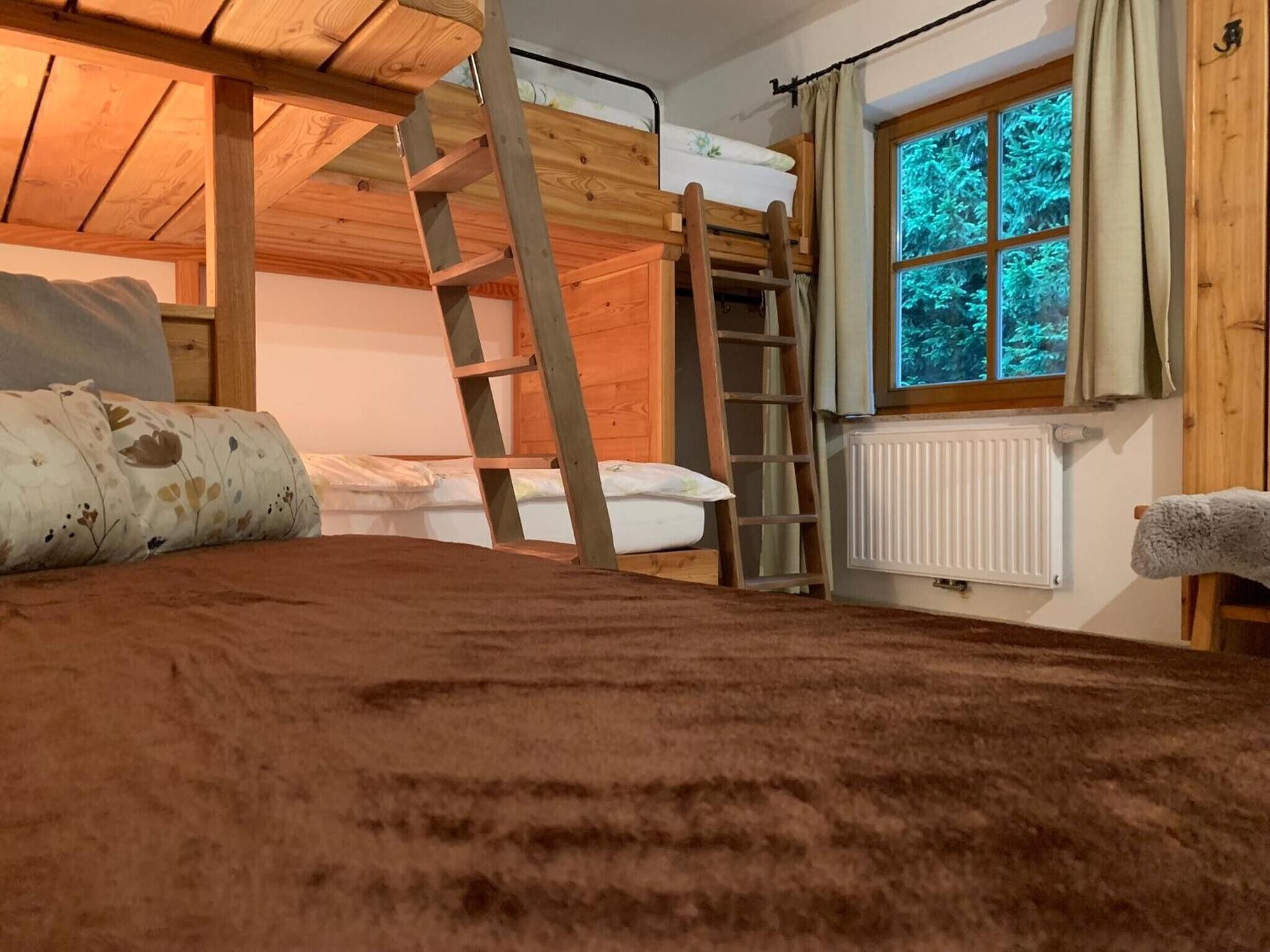 A bunk bed room with a wooden ladder, a window with curtains, and a radiator.