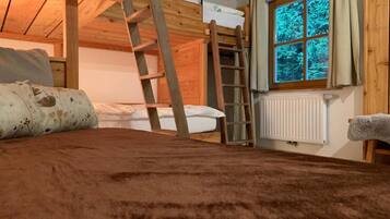A bunk bed room with a wooden ladder, a window with curtains, and a radiator.