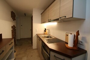 A kitchen with wooden cabinets, a stainless steel sink, and a wooden cutting board with a paper towel holder.