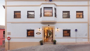 Un edificio de dos pisos con fachada simétrica, una entrada central con escaleras y dos banderas en la parte superior.
