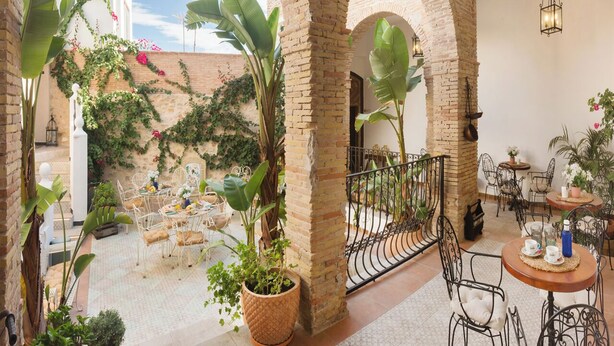 Un patio al aire libre con arcos de ladrillo, plantas en macetas y mobiliario de metal.