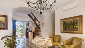 Un vestíbulo amplio con piso estampado, una escalera, un candelabro y un cuadro grande.
