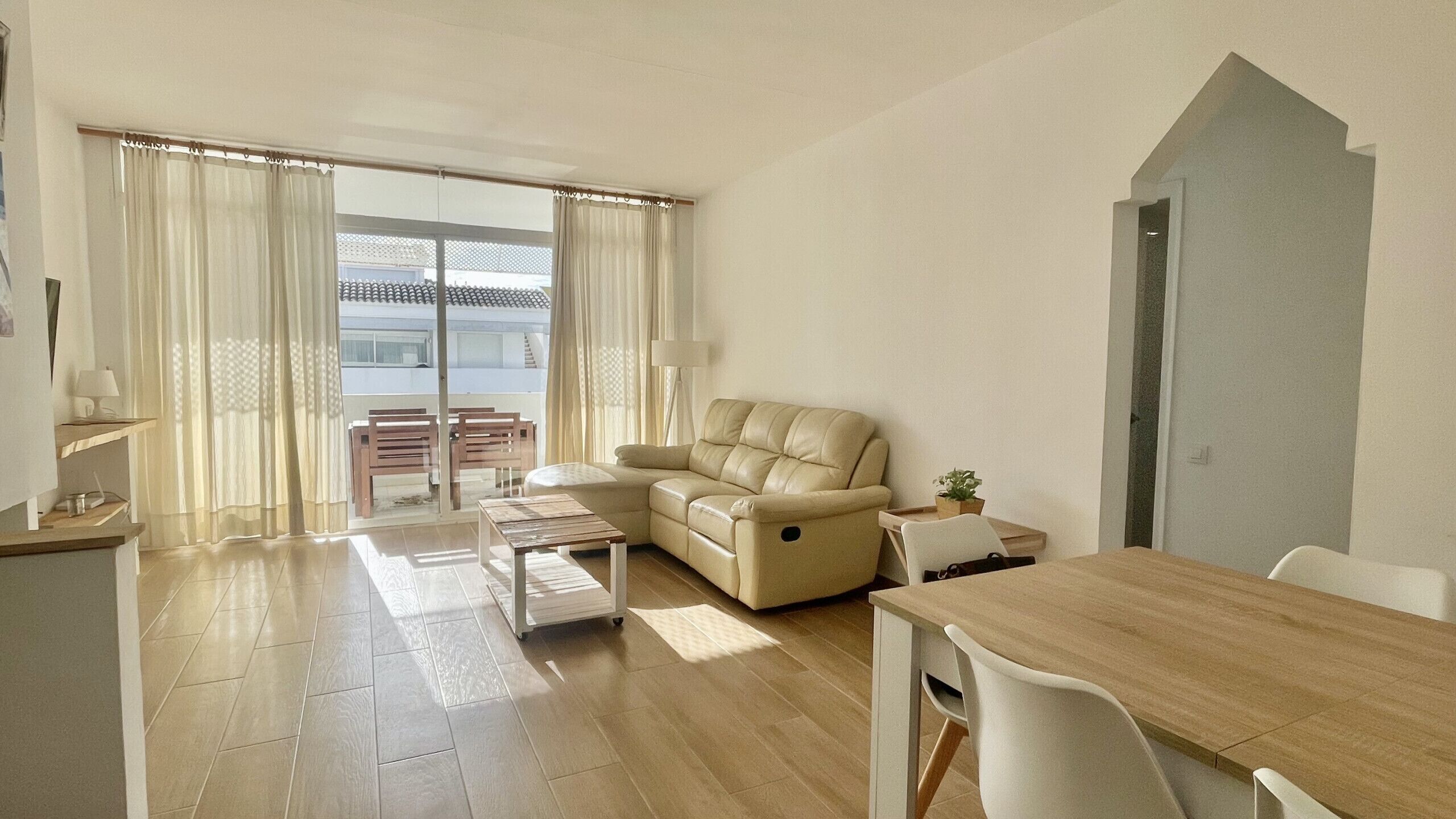 Ein Wohnzimmer mit einer Couch, einem Esstisch und Blick durch eine Glastür auf einen Balkon.