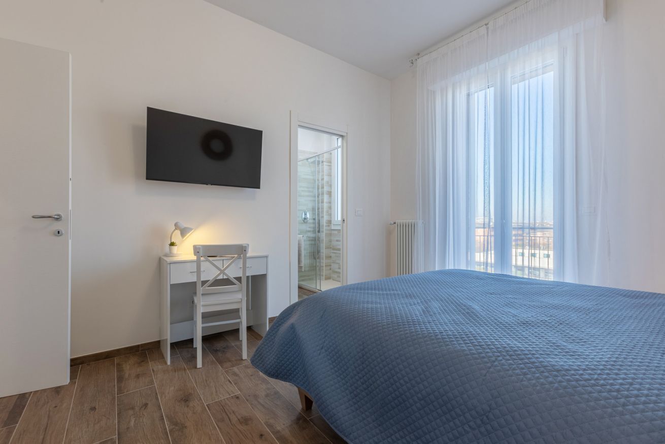 Ett sovrum med en säng, ett skrivbord, en stol, en tv och ett fönster med gardiner.