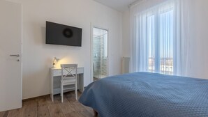 Ein Schlafzimmer mit Bett, Schreibtisch, Stuhl, Fernseher und einem Fenster mit Vorhängen.