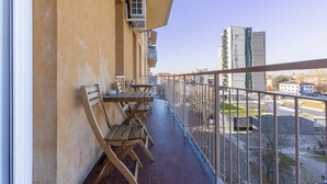 Ein Balkon mit Holzkubeln und Tischen, Klimaanlagen und Blick auf eine Stadtlandschaft, darunter ein hohes Gebäude mit der Aufschrift 'POWER'.