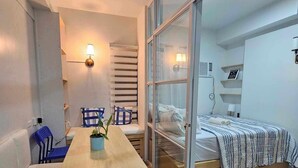 Une chambre moderne avec un bureau en bois, un lit recouvert d’une courtepointe à rayures, un ventilateur de plafond et une grande fenêtre.