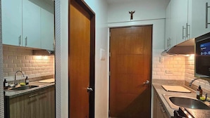 Une cuisine compacte avec des meubles blancs, une porte en bois, un four encastré et une petite fenêtre.