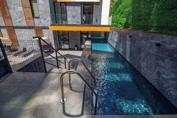Enjoy a refreshing swim in the pool surrounded by a stone wall and glass facade.