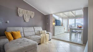 A living room with a grey sofa, yellow cushions, a knitted throw, and macrame wall art. - Sea view terrace close to the beach of Lido di San Giovanni in Alghero (Alghero)