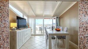A modern dining area with a TV, dining table, chairs, and a view of the sea. - Sea view terrace close to the beach of Lido di San Giovanni in Alghero (Alghero)