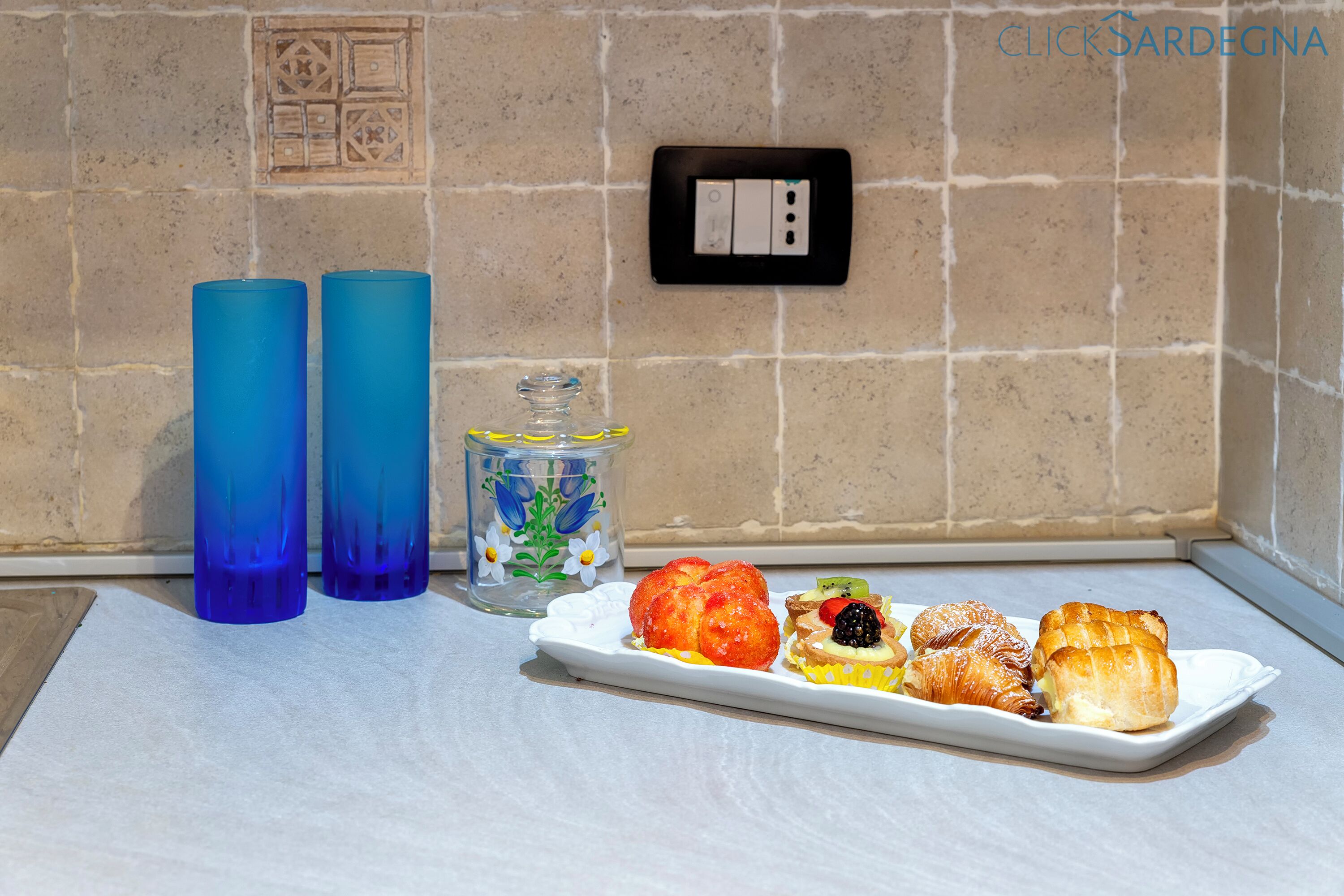 A kitchen counter with a plate of pastries, two blue tumblers, and a decorative glass jar.