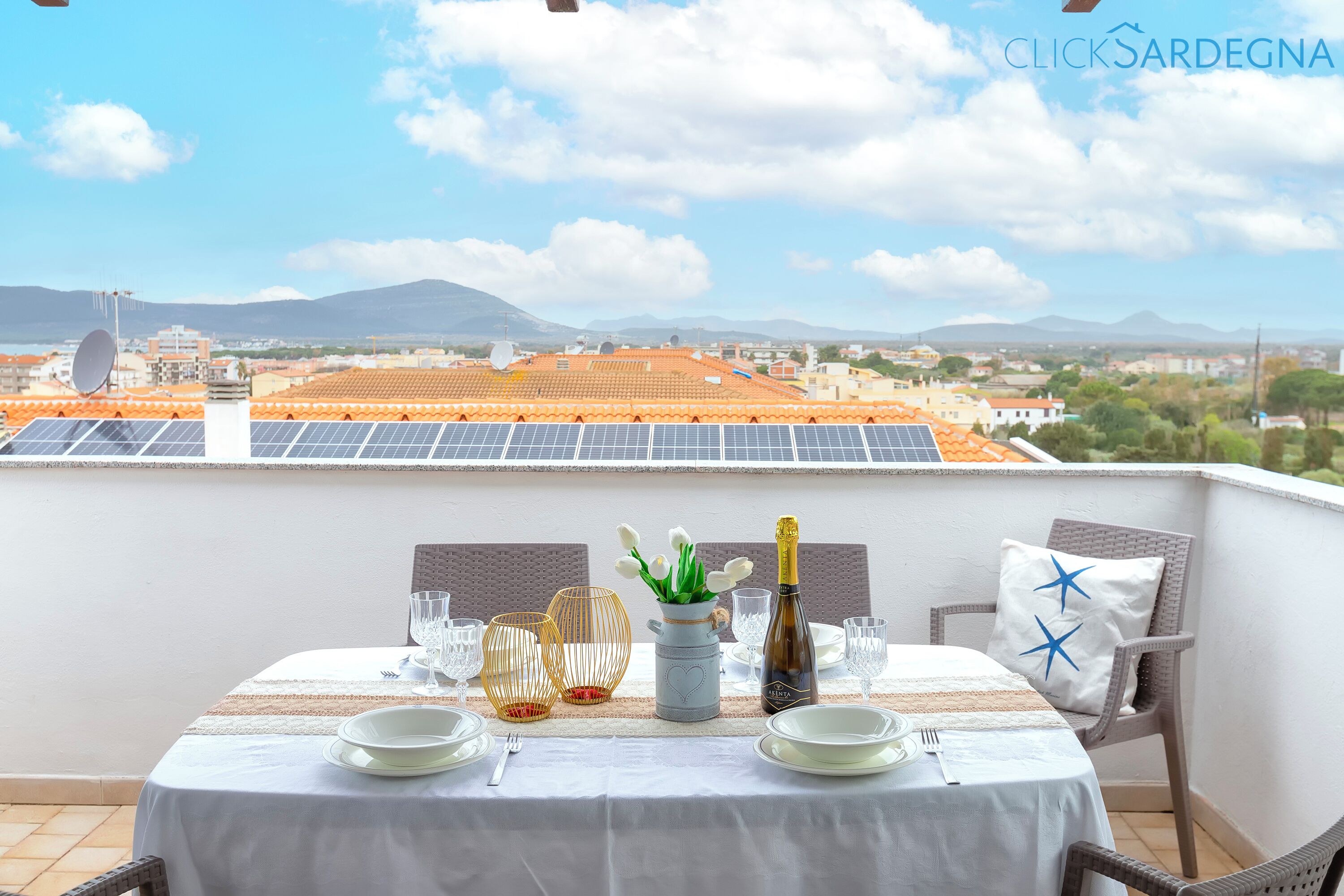 A table set for dining on a balcony with a view of solar panels and buildings in the distance.