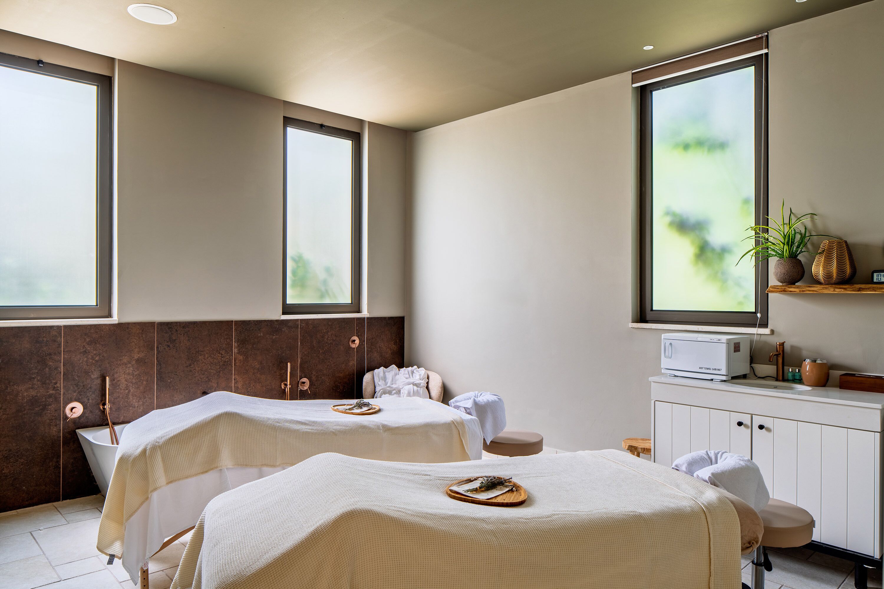 Un cuarto de spa con dos camillas de masaje, una bañera y un mueble pequeño con microondas.