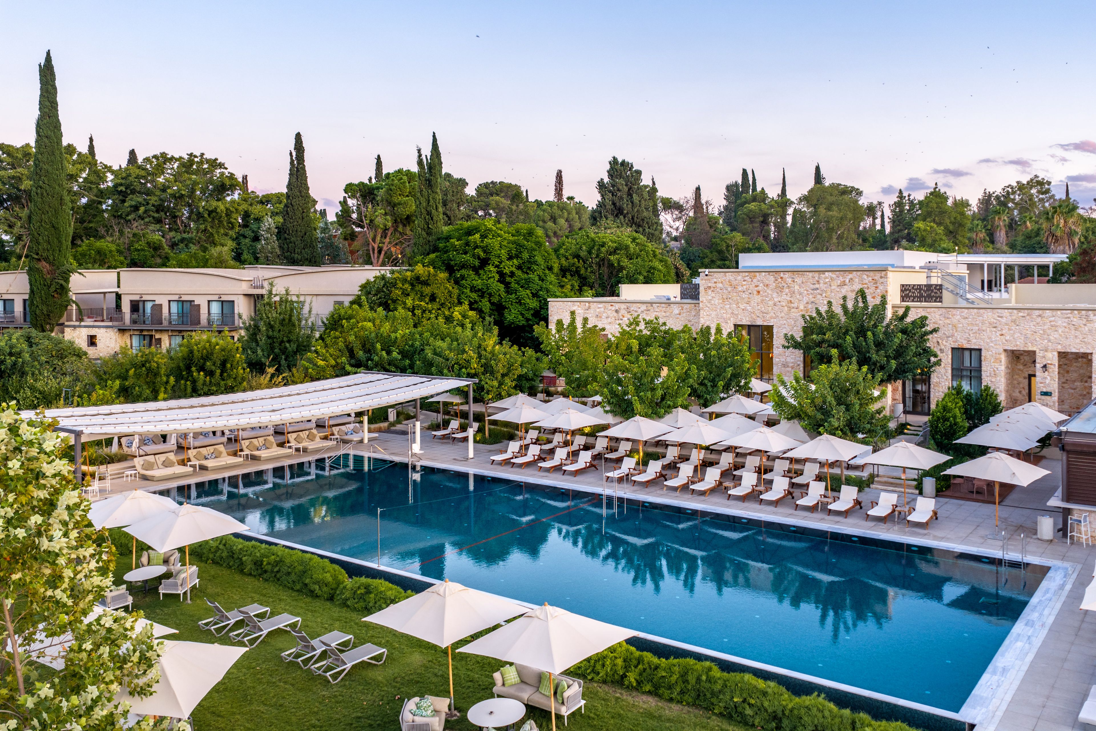 A swimming pool with lounge chairs and umbrellas, surrounded by greenery and buildings.