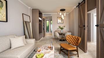 Una sala de estar moderna con un sofá, una mesa de centro con frutas y bebidas, una zona de comedor con mesa y sillas, y un gran ventanal corredero.
