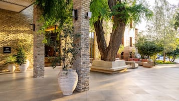 A courtyard with stone pillars, large potted plants, and outdoor seating.