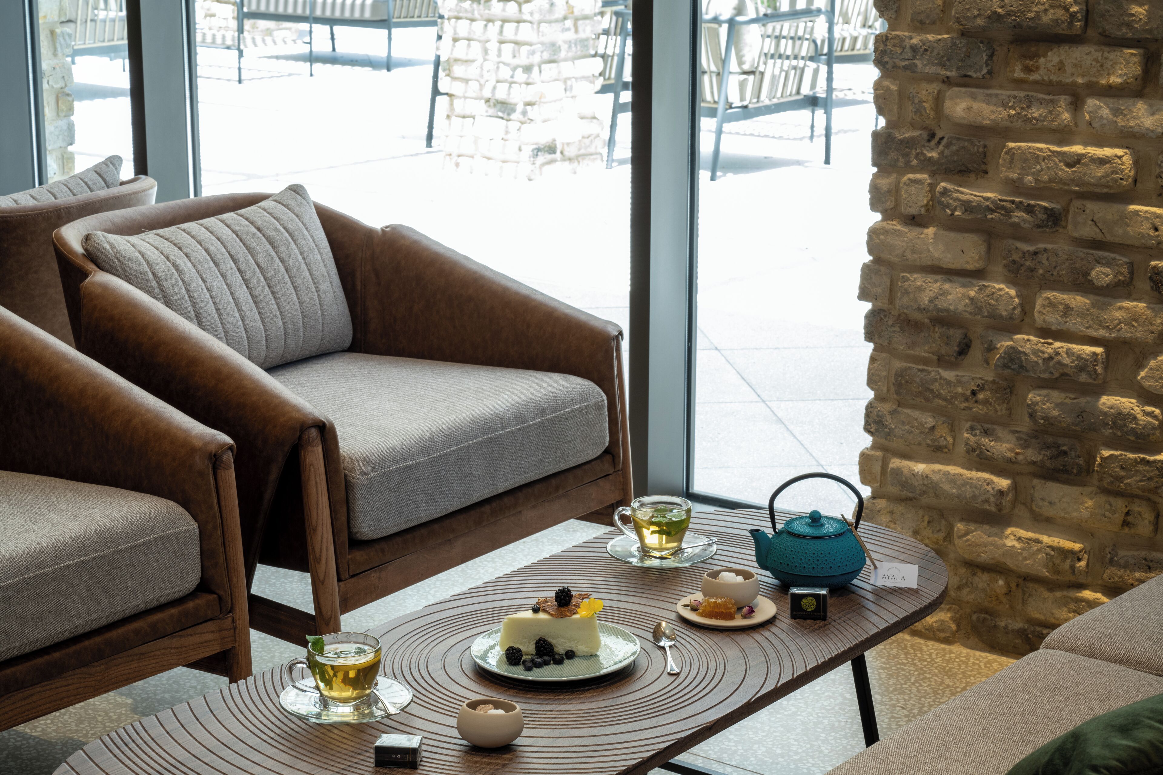 A cozy seating area with a sofa and armchairs, a table with a cake and tea, and a view of the outdoor seating area.