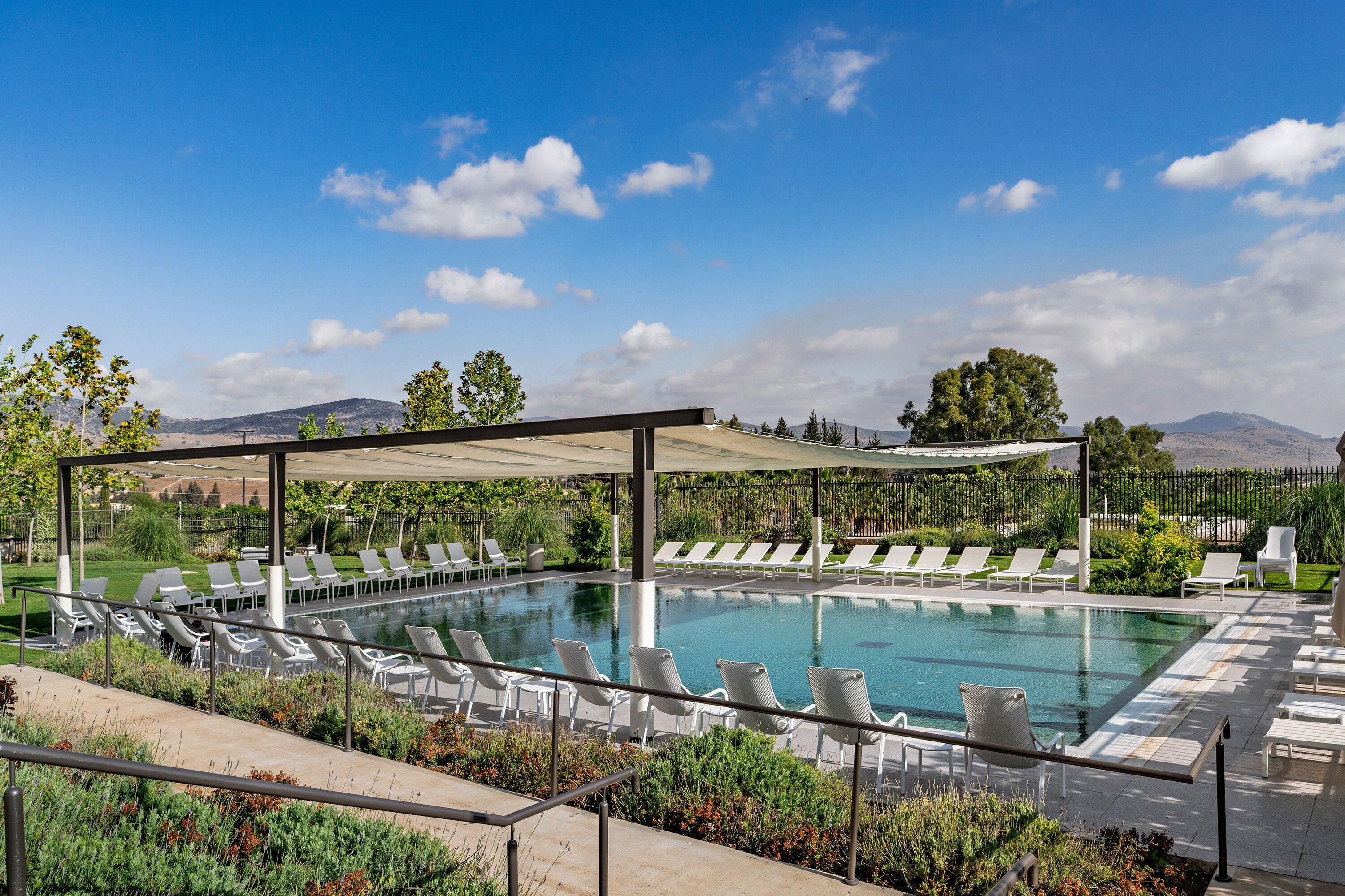 A pool area with sun loungers and a covered seating area, surrounded by greenery and mountains in the background.