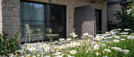 A stone building with a patio area featuring green chairs and a flower bed with white daisies.